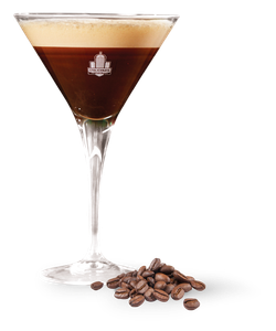 Das Glas zeigt ein schokoladiges Getränk mit einer cremigen Schicht, während geröstete Kaffeebohnen im Vordergrund liegen.