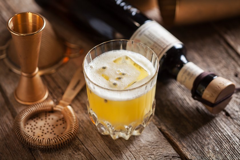 Ein Glas mit einem gelben Getränk, das mit Eiswürfeln gefüllt ist, steht auf einer rustikalen Holzoberfläche.