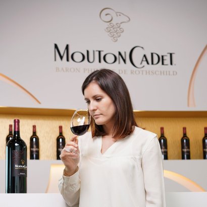 Die Frau mit langen, braunen Haaren hält ein Glas Rotwein und scheint den Duft des Weins zu genießen, umgeben von einer stilvollen Bar.