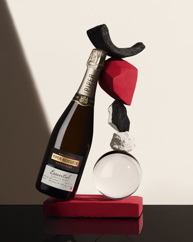 Eine stilvolle Anordnung zeigt eine Flasche Piper-Heidsieck Champagner, balanciert auf einer roten Fläche mit verschiedenen dekorativen Elementen.