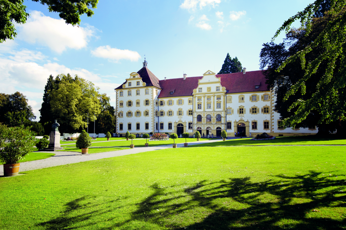 Im Vordergrund sind grüne Rasenflächen und dekorative Pflanzen zu sehen, die das eindrucksvolle Schloss im Hintergrund umrahmen.
