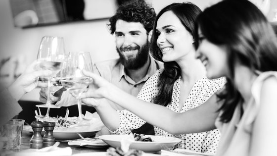 Eine Gruppe von Freunden hebt ihre Gläser in einem fröhlichen Toast während eines gemeinsamen Essens in einem Restaurant.