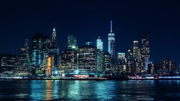 Die Skyline einer Stadt erstrahlt nachts mit leuchtenden Wolkenkratzern und reflektiert im ruhigen Wasser des Hafens.