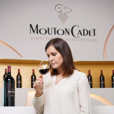 Die Frau mit langen, braunen Haaren hält ein Glas Rotwein und scheint den Duft des Weins zu genießen, umgeben von einer stilvollen Bar.