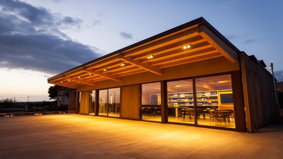 Ein modernes Gebäude mit großen Fenstern, das bei Dämmerung beleuchtet ist und eine einladende Atmosphäre ausstrahlt.