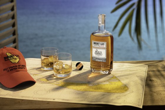 Zwei Gläser mit eisgekühltem Rum und eine Flasche stehen auf einer Seekarte, während ein Hut und das blaue Meer im Hintergrund sichtbar sind.