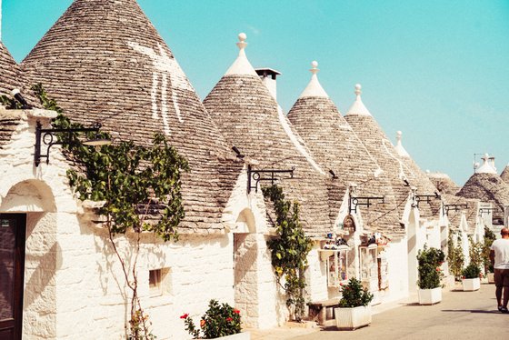Eine malerische Straße mit traditionellen Trulli-Häusern, deren kegelförmige Dächer aus grauen Steinen bestehen.