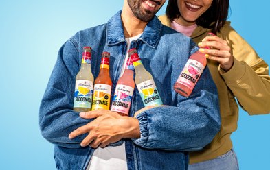 Die Secconade Flaschen in den Händen der beiden Personen strahlen in lebhaften Farben und vermitteln ein Gefühl von Freude.