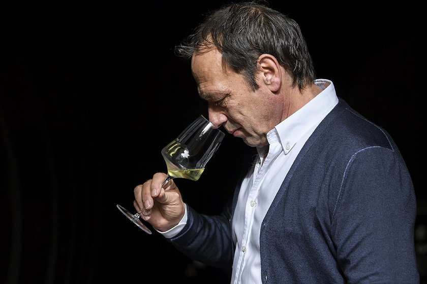 Der Mann mit dem kurzen Haar und dem blauen Cardigan beugt sich über sein Glas, um den Wein sorgfältig zu riechen.
