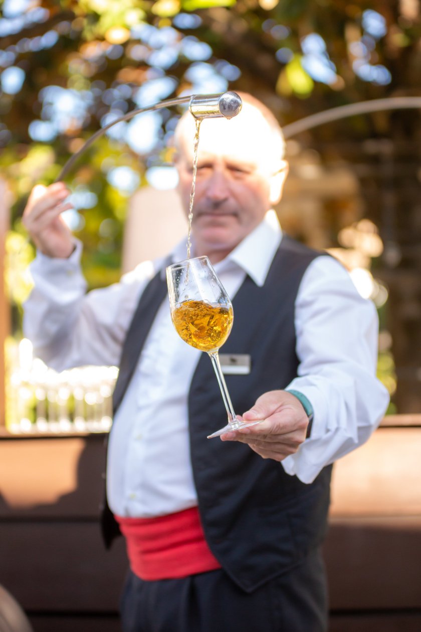 In einem schönen Außenbereich gießt ein Kellner mit einem geschickten Handgriff ein Getränk in ein Glas, das er hält.