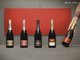 Fünf Flaschen Champagner von Piper-Heidsieck stehen auf einem grauen Tisch vor einer roten Wand.
