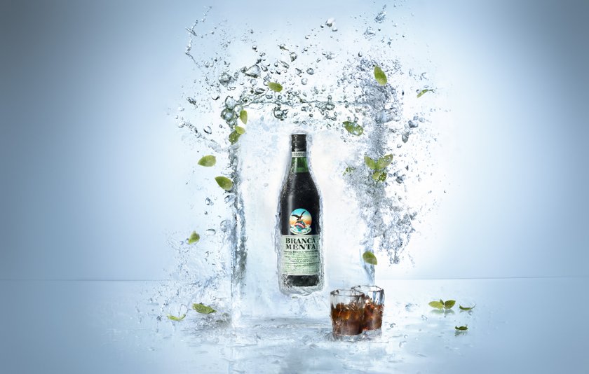 Die Flasche Branca Menta wird von Wasser und Minzblättern umgeben, was eine erfrischende Atmosphäre schafft.