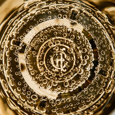 Ein Blick auf die Blasen in einem Glas Champagner, das die glänzende Oberfläche und das Logo im Inneren zeigt.