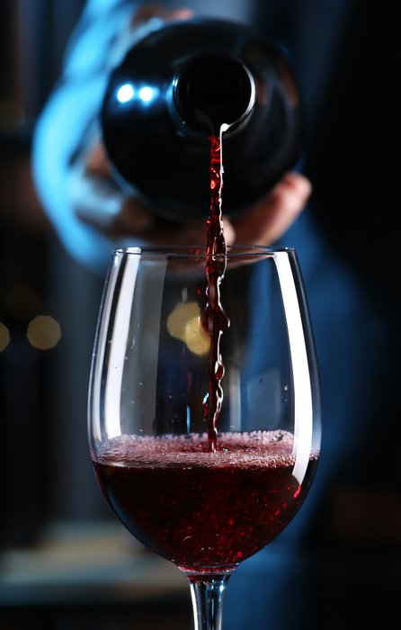 Ein Glas wird mit tiefrotem Wein gefüllt, während eine Hand die Flasche mit einem eleganten Schwung hält.