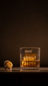 Ein elegantes Glas mit goldenem Getränk steht auf einem Tisch, daneben liegt ein goldener Korken mit der Aufschrift 1866.