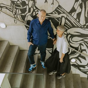 Ein Mann und eine Frau stehen auf einer Treppe, umgeben von einer auffälligen Wandmalerei in Schwarz-Weiß.