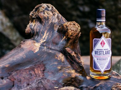Eine Flasche Westland Whiskey steht auf einem rustikalen Holzstück, das die natürliche Maserung und Textur zeigt.