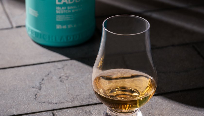 Ein elegantes Glas mit goldenem Whisky steht auf einem grauen Steinboden, während eine Flasche Bruichladdich im Hintergrund sichtbar ist.