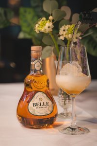 Ein elegantes Glas mit einem Cocktail, gefüllt mit Eis und Lavendel, wird von einer Flasche Belle de Brillet begleitet.