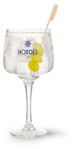 Ein elegantes Glas mit Nordés Gin, gefüllt mit Eis und zwei leuchtend gelben Oliven, steht auf einem dunklen Untergrund.