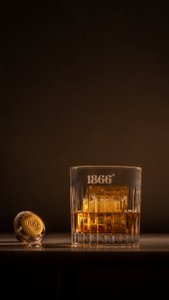 Ein elegantes Glas mit goldenem Getränk steht auf einem Tisch, daneben liegt ein goldener Korken mit der Aufschrift 1866.
