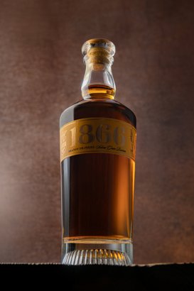 Eine elegante Flasche Brandy mit dem Jahr 1866 auf dem Etikett, vor einem warmen, braunen Hintergrund platziert.