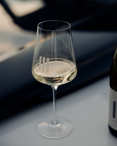 Das Glas mit dem klaren Weißwein reflektiert das Licht, während eine Flasche Wein daneben platziert ist.