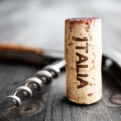 Ein Korken mit der Aufschrift 'ITALIA' steht auf einem dunklen Holztisch, umgeben von einem Korkenzieher.