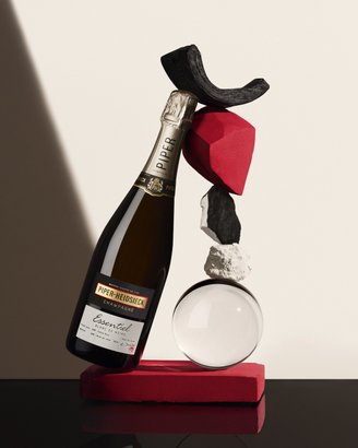 Eine stilvolle Anordnung zeigt eine Flasche Piper-Heidsieck Champagner, balanciert auf einer roten Fläche mit verschiedenen dekorativen Elementen.