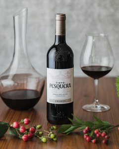 Eine Flasche Tinto Pesquera steht auf einem Holztisch, umgeben von einem Weinglas und frischen Beeren.