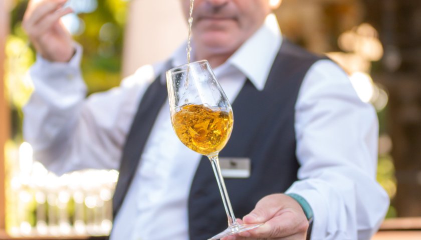In einem schönen Außenbereich gießt ein Kellner mit einem geschickten Handgriff ein Getränk in ein Glas, das er hält.