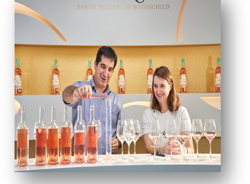 Hinter einem stilvollen Tresen füllt ein Mann Wein in Gläser, während eine Frau mit einem Lächeln die Szene genießt.