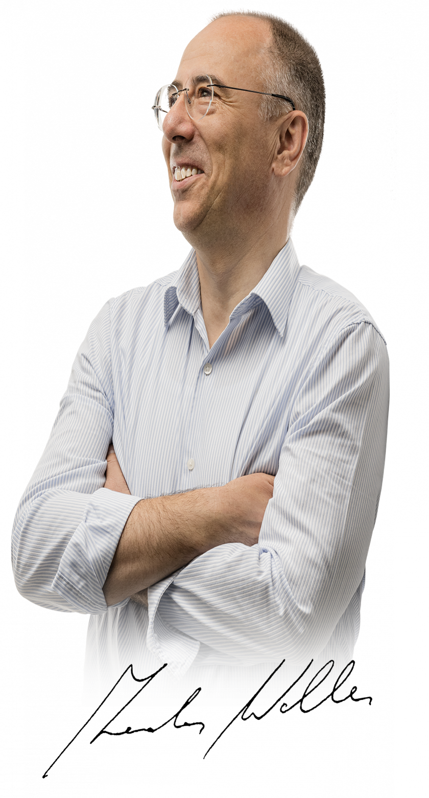 In einem hellblauen gestreiften Hemd steht ein Mann mit verschränkten Armen und einem freundlichen Ausdruck auf dem Gesicht.