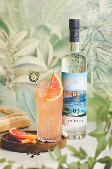 Ein erfrischender Cocktail mit einer Scheibe Grapefruit und Eiswürfeln, serviert in einem Glas neben einer Flasche Humboldt Gin.