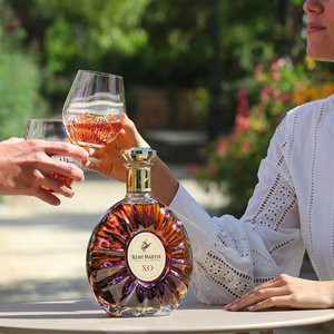 Zwei Personen stoßen mit Gläsern an, während eine elegante Flasche Rémy Martin XO im Vordergrund steht.