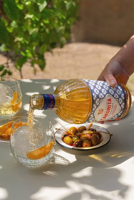 Ein Glas wird mit einem goldenen Getränk gefüllt, während eine Hand die Flasche mit dem Etikett 'Canonita' hält.