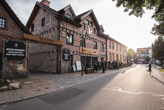 Ein historisches Gebäude mit Backsteinfassade und Holzverzierungen, das eine Destillerie beherbergt, ist im Vordergrund sichtbar.