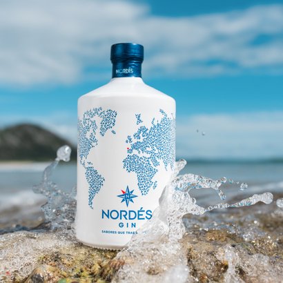 Eine stilvolle Gin-Flasche steht auf einem Felsen, während Wellen spritzen und die Sonne am Himmel scheint.