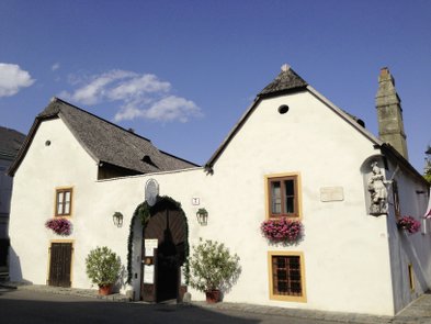 Ein charmantes, weißes Gebäude mit einem geschwungenen Dach und bunten Blumen an den Fenstern, unter einem blauen Himmel.