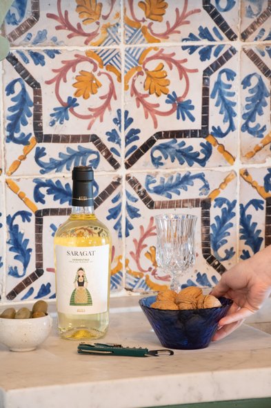 Eine Flasche Saragat Vermentino steht neben einem eleganten Glas und einer Schale mit Walnüssen auf einer marmorierten Oberfläche.