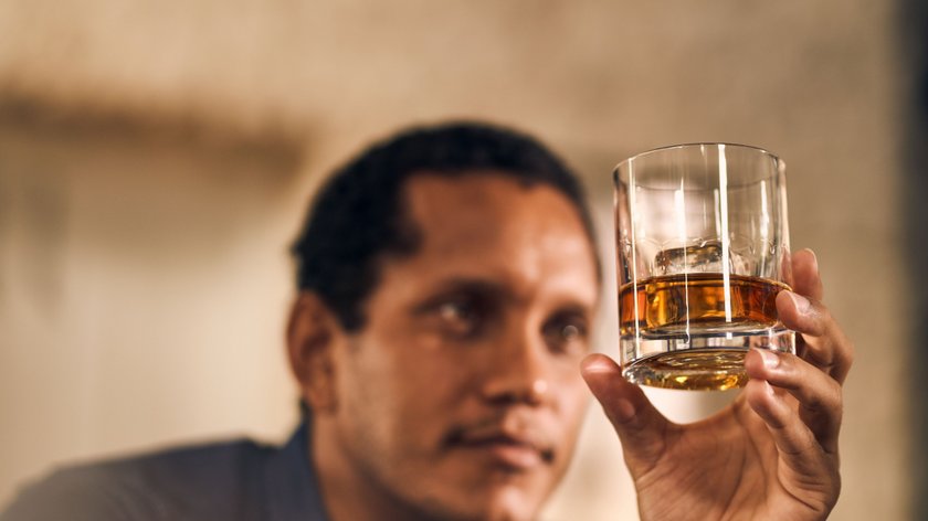 Ein Mann betrachtet nachdenklich ein Glas mit Whiskey, während er die Farbe des Getränks bewundert.