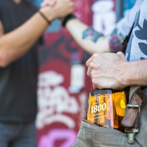 Zwei Personen schütteln sich die Hände, während eine Flasche Tequila 1800 Reposado in der Tasche des einen sichtbar ist.
