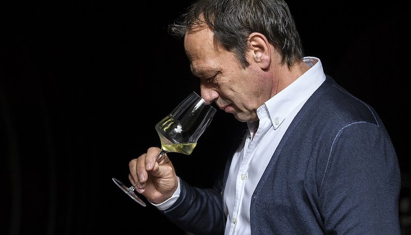 Der Mann mit dem kurzen Haar und dem blauen Cardigan beugt sich über sein Glas, um den Wein sorgfältig zu riechen.