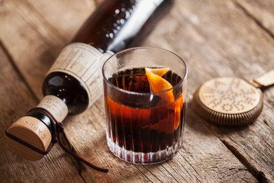 Ein Glas mit dunklem Getränk, garniert mit Orangenscheiben, steht auf einer rustikalen Holzoberfläche.