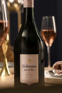 Eine elegante Flasche Geldermann Grand Rosé steht im Vordergrund, umgeben von Gläsern und einem gedeckten Tisch.