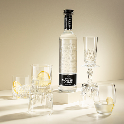Eine elegante Flasche Tequila steht neben mehreren Gläsern, einige mit Zitronenscheiben dekoriert, auf einem hellen Tisch.