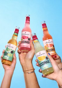 Vier Hände halten bunte Flaschen mit Erfrischungsgetränken vor einem strahlend blauen Himmel.