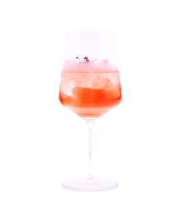 Zart rosafarbener, perlender Drink mit Eiswürfeln, einer dichten Schaumkrone und kleinen roten Blütenblättern in einem hohen Stielglas vor weißem Hintergrund.
