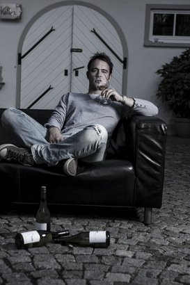 Ein Mann sitzt entspannt auf einem schwarzen Sofa, während er ein Glas Wein genießt und nachdenklich in die Ferne blickt.