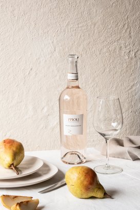 Ein elegantes Arrangement aus einer Flasche rosé Wein, einem Glas und reifen Birnen auf einem hellen Tisch mit sanfter Textur.